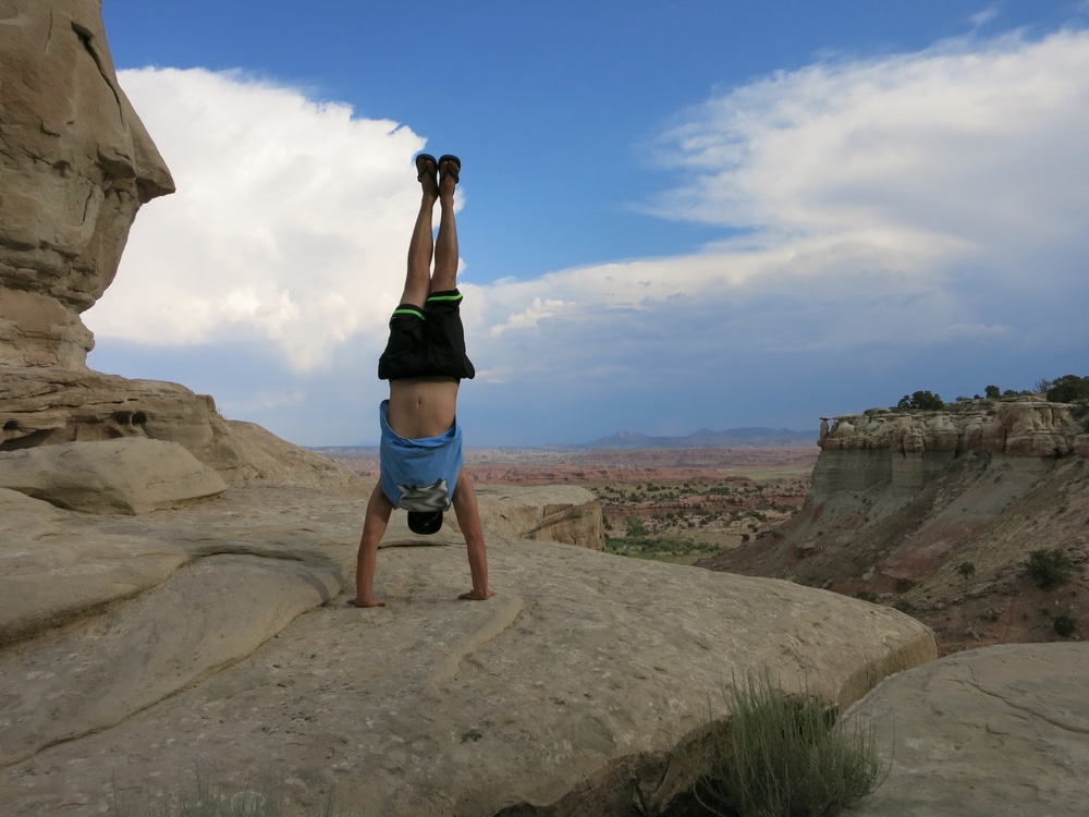 Man does Handstand on cliffs with field landscape in the desert